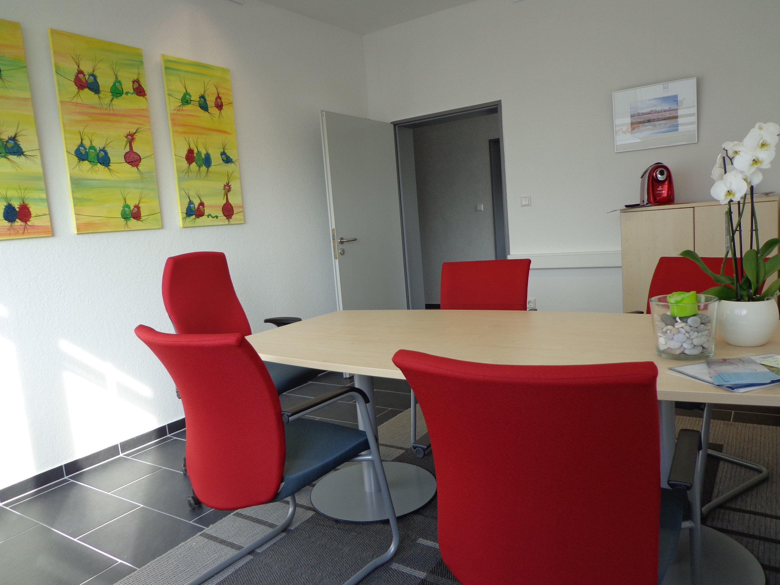 Das schöne Büro von Stebner Immobilien von innen, 5 rote Stühle, ein Eckiger Tisch in der Mitte. Es hängen gelbe Bilder an der Wand.